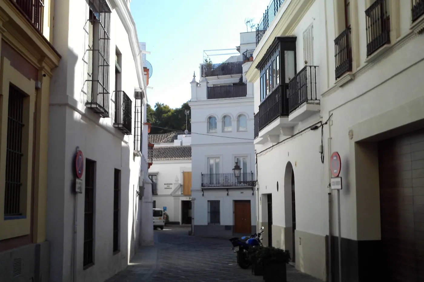 A narrow whitewashed street, Calle Dean Miranda, with wrought-iron balconies and a glassed-in gallery