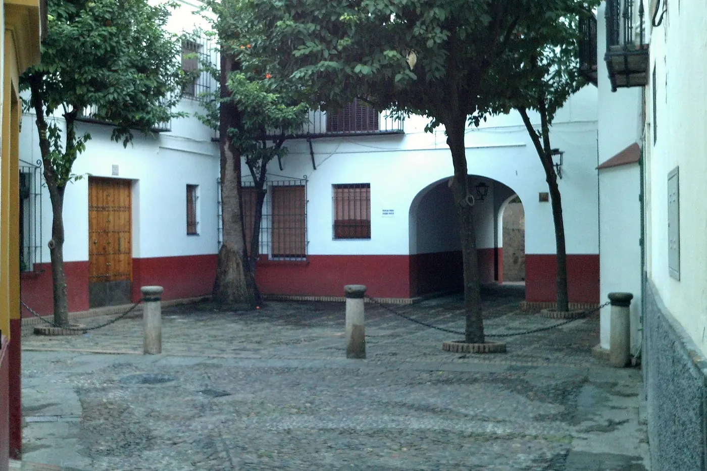 A small cobbled square on Calle Susona with trees, whitewashed walls with a red base and an arched passage