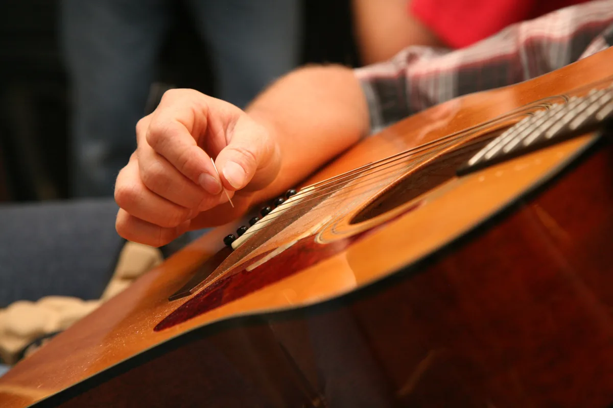 A guitarist's right hand over the strings of a guitar with a warm orange top, seen close up