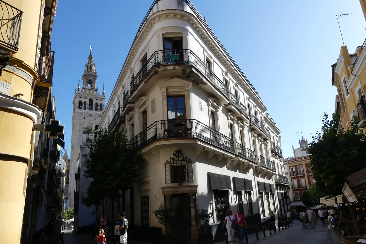 A street corner in central Seville with a balconied corner building and the Giralda tower rising behind it